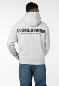 Grau Hoodie mit großen schwarzen Buchstaben "WORLDWIDE" auf der Rückseite, gerippten Bündchen und einer Kängurutasche. Mit einer Kapuze mit Kordelzug.