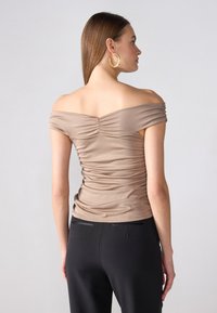 Bežs off-the-shoulder tops, kam aizmugurē un gurnos ir rūtika. Kopa ar melniem biksēm ar gludu tekstūru un pieguļošu dizainu.
