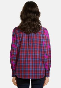 Košile s červeným a modrým kárem, která má dlouhé rukávy zdobené růžovou květinovou výšivkou, v uvolněném střihu a s zaobleným lemem.