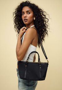 Borsa a mano nera in nylon con doppi manici e tracolla rimovibile, caratterizzata da hardware dorato e chiusura con zip. Dettagli testurizzati sulle cinghie.