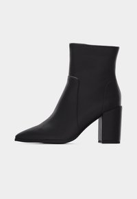 Μαύρο δερμάτινο μποτάκι αστραγάλου με μυτερή μύτη και χοντρό ψηλό τακούνι, με λεία επιφάνεια και ελάχιστες ραφές, παρουσιάζεται σε απλό φωτεινό φόντο.