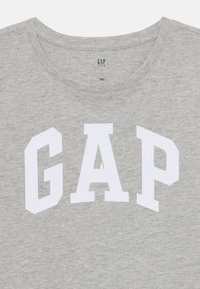 T-shirt gris à manches courtes en coton avec col rond. Présente un lettrage "GAP" en relief blanc sur le devant.