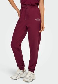 Maroon flis pantalone s elastičnom trakom u struku i vezicom, bočne džepove, manžete na gležnjevima i bijeli detalj s natpisom "Athleisure".