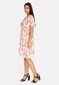 Blommig klänning i mjuk rosa med korta ärmar, åtsmitande midja och en flödande kjol. Matchad med svarta högklackade sandaler.