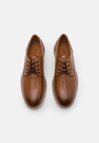 Un paio di scarpe eleganti in pelle marrone lucida con lacci neri e cuciture beige su uno sfondo bianco.