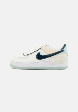 Niskie białe sneakersy z jasnoniebieskimi akcentami, czarnym logo Nike swoosh, sznurowanym zapięciem i gruba podeszwą z logo "AIR" z boku.
