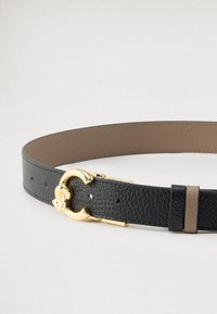 Juodas odinis diržas su tekstūruota paviršiaus apdaila, featuring auksinio tono sagtį ir rudos odos detalę šalia sagties.