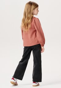 Rosa kariertes Langarmoberteil, kombiniert mit schwarzen weit geschnittenen Jeans und rot-weißen Sneakers mit schwarzem Finish und strukturierter Oberfläche.