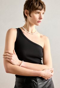 Svart ribbet tanktop med én skulder, kombinert med et hvitt perlekjede og perlearmbånd, med en glatt tekstur og tettsittende design.