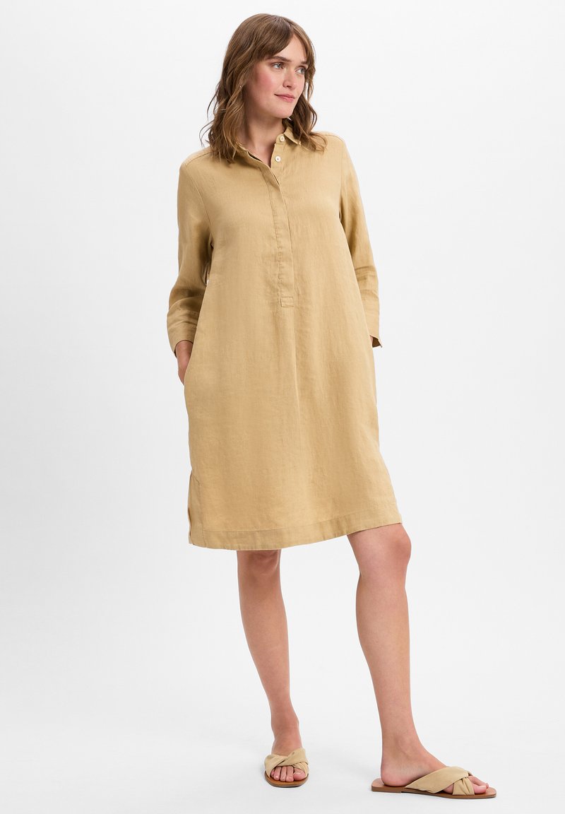 Langarmige jurk met kraag in zacht beige linnen. Bevat een knoopsluiting, zijzakken en een ontspannen A-lijn silhouet. Verfraaid met minimale stiksels.