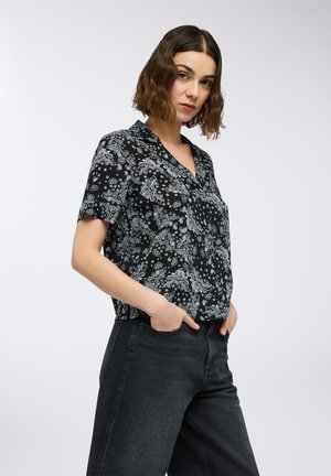 Camicetta nera a maniche corte con motivo floreale paisley bianco, colletto, vestibilità rilassata. Abbinata a jeans in denim scuro.