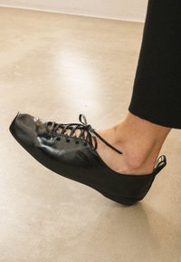 Scarpe in pelle nera con punta arrotondata, lacci frontali e retro aperto. Presentano una texture liscia e una finitura lucida discreta.