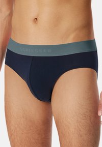 Marineblaue Herrenunterhosen mit glatter Textur, ausgestattet mit einem hellgrauen elastischen Bund mit eingeprägtem "Schiesser"-Logo.