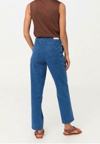 Light brown sleeveless top with blue denim high-waisted pants. Pants feature two back pockets and a straight leg cut. Brown sandals.