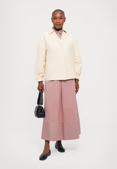 Κρέμα μπλούζα με φουσκωτά μανίκια, κουμπωτή. Ανοιχτό ροζ midi φούστα με ραφή, συνδυασμένη με μαύρες μπαλαρίνες και μια μικρή καπιτονέ μαύρη τσάντα.