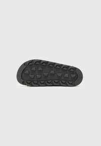 Svart gummisåle med teksturerte ribber og lugs for grep, med en glatt senterseksjon og distinkte mønstre for trekkraft.