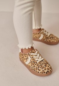 Leopardmönstrade sneakers med vit snörning och sidodetaljer, med en mjuk yta och en brun gummisula, i kombination med ribbade vita leggings.