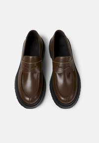 Mocasines de cuero marrón con acabado liso, suela de goma negra, puntera redondeada y una correa decorativa en la parte media.