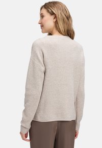 Beżowy sweter o teksturowanej powierzchni, luźnym kroju i długich rękawach. Wykonany z miękkiego materiału z delikatnymi błyszczącymi detalami, z okrągłym dekoltem.