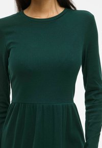 Robe verte côtelée avec un col rond et des manches longues, dotée d'un corsage ajusté et d'une jupe évasée. Texture douce et matériau très extensible.