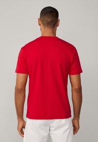 Camiseta corta de manga corta roja con cuello redondo y textura suave, que presenta un diseño limpio en la parte trasera. El material parece ligero y transpirable.