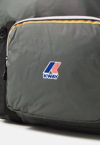 Bolsa de tejido gris con textura y un bolsillo con cremallera, que presenta un colorido logo de K-Way y un ribete en amarillo, rojo y azul.