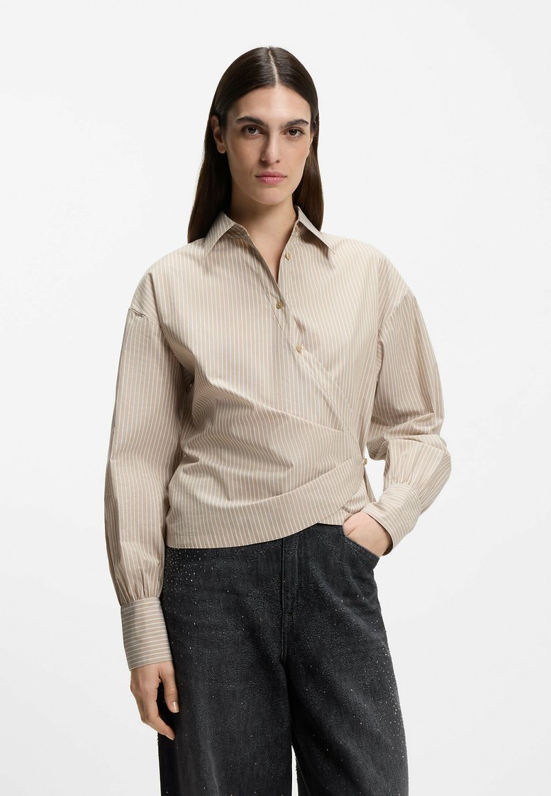 Beżowa koszula w paski z kołnierzykiem, plisą na guziki i długimi rękawami. Noszona z ciemnymi, lekko fakturowanymi, wysokim stanem spodniami.