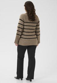 Pull en laine rayé marron avec un ourlet côtelé, présentant des rayures noires. Porté avec un pantalon noir et des chaussures élégantes. Vue de dos montrée.