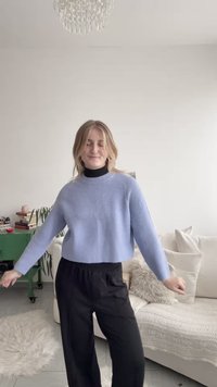 Ljusblå kort tröja med ribbad struktur och långa ärmar, kombinerad med svarta vida byxor, i en ljus inomhusmiljö.