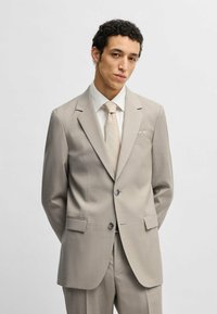 Completo beige chiaro con finitura testurizzata, caratterizzato da una giacca a due bottoni e revers a punte, abbinato a una cravatta coordinata e una camicia bianca.