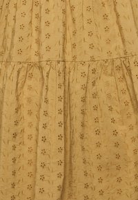 Tecido de algodão amarelo mostarda com padrões florais bordados e bordas em forma de concha. Apresenta detalhes franzidos e uma superfície texturizada.