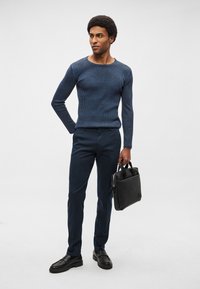 Mörkblå ribbstickad tröja med rund halsringning, kombinerad med mörkblå smala byxor. Svart läderväska och svarta slip-on skor fulländar looken.