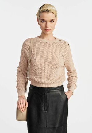 Jasno beżowy sweter dzianinowy z okrągłym dekoltem, długimi rękawami i guziczkami na ramionach. Połączony z czarną skórzaną spódnicą i jasnobrązową torebką na biodro.