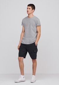 Grå kortærmet T-shirt parret med sorte cargo shorts med sidelommer, iført hvide højhalsede sneakers. Enkel design og afslappet pasform.