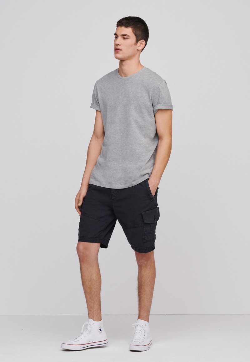 Grå kortærmet T-shirt parret med sorte cargo shorts med sidelommer, iført hvide højhalsede sneakers. Enkel design og afslappet pasform.