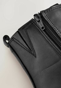 Black leather glove featuring a side zipper, textured surface, and angled cut near the wrist, accented with visible stitching details.