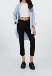 Světle modrá oversized košile, bílý crop top, černé slim-fit kalhoty a robustní černé mokasíny. Košile má ohrnuté rukávy.