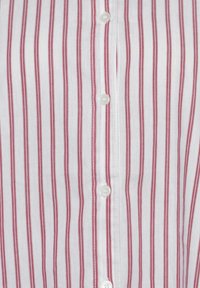 White button-up shirt with narrow red stripes, featuring white buttons and a smooth cotton texture.