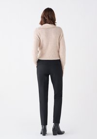 Suéter de punto beige con cuello, combinado con pantalones negros de corte ajustado. El atuendo presenta un ajuste relajado y texturas suaves, con botas a la altura del tobillo.