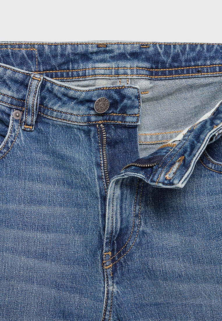 Jean en denim bleu dézipé avec fermeture éclair, bouton, passants de ceinture et couture orange sur un fond blanc.