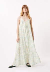 Robe maxi de couleur vert pâle, ornée d'un motif géométrique bleu et jaune, avec un décolleté en V et un ourlet froncé. Le mannequin porte des ballerines noires.