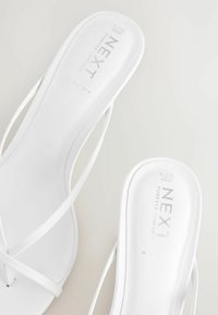 Une paire de sandales blanches à brides pour femmes avec des semelles plates, arborant la marque "NEXT Forever Comfort" et des détails de taille à l'intérieur.
