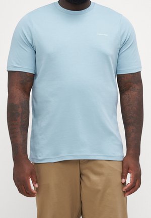 Lyseblå bomuld T-shirt med korte ærmer og rund hals. Har en lille hvid "Calvin Klein"-logo på øverste venstre bryst.