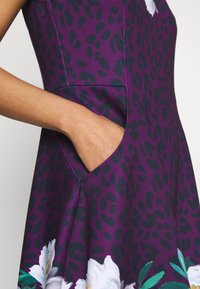 Lila klänning med svart leopardtryck, med ett blommönster vid fållen. Inkluderar en sidficka och ett mjukt, texturerat tyg.