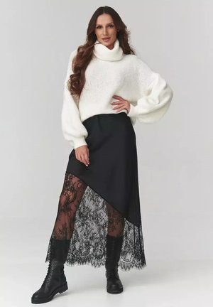 Biały sweter z dzianiny z wysokim kołnierzem, w parze z czarną asymetryczną spódnicą z koronkowym wykończeniem oraz czarnymi butami wojskowymi.