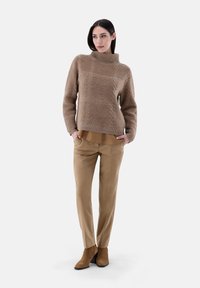 Beige gestrickter Pullover mit hohem Kragen und strukturiertem Muster. Kombiniert mit hellbraunen maßgeschneiderten Hosen und taupefarbenen Stiefeletten. Schlichte, neutrale Farbpalette.
