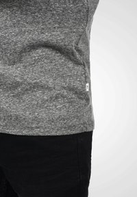 Camiseta gris jaspeada hecha de una tela suave, con escote redondeado, mangas cortas, que presenta una pequeña etiqueta blanca en la costura lateral.