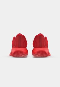 Røde atletiske sko med en struktureret gummisål, glat stofoverdel og polstret hæl. Vist i et bagudsigt, der fremhæver designstrukturen.