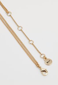 Collier en chaîne dorée avec des maillons entrelacés, un fermoir en forme de homard et une étiquette ronde gravée. Texture lisse et finition brillante.