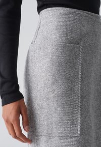 Falda de lana gris con un patrón de espiga, que cuenta con un bolsillo lateral y una cinturilla suave. La tela parece cálida y texturada.